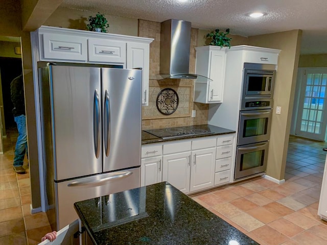 kitchen featuring backsplash, wall chimney exhaust hood, a textured ceiling, white cabinetry, and stainless steel appliances