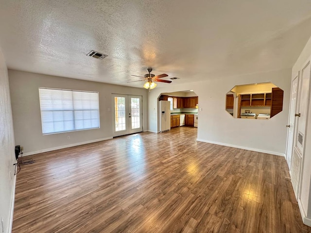 unfurnished living room featuring arched walkways, dark wood-style flooring, visible vents, a textured ceiling, and baseboards