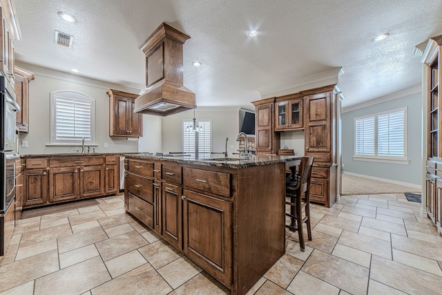 kitchen featuring a kitchen breakfast bar, a center island with sink, a textured ceiling, and ornamental molding