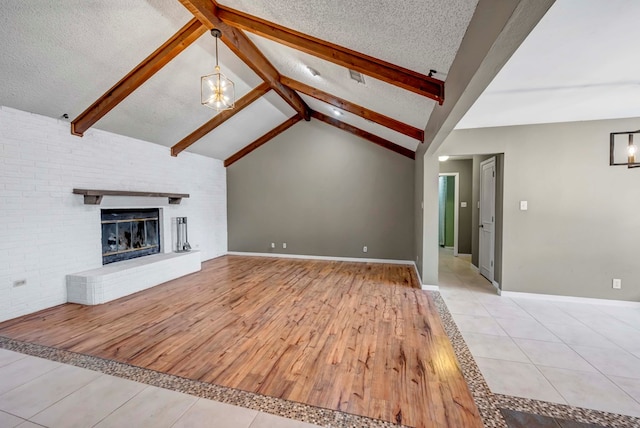 unfurnished living room with light wood-type flooring, a textured ceiling, vaulted ceiling with beams, and a brick fireplace