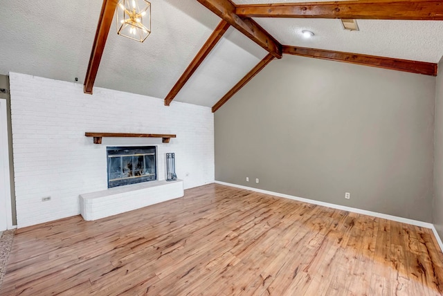 unfurnished living room featuring an inviting chandelier, light hardwood / wood-style flooring, lofted ceiling with beams, a textured ceiling, and a fireplace