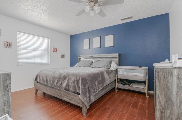 bedroom with a ceiling fan, wood finished floors, visible vents, and a textured ceiling