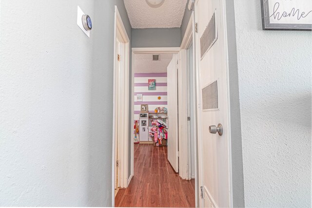 hall featuring a textured ceiling, a textured wall, and wood finished floors