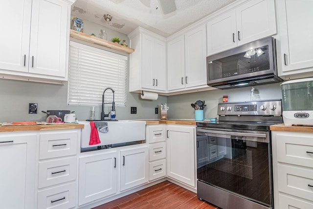 kitchen with light countertops, appliances with stainless steel finishes, wood finished floors, white cabinetry, and a sink