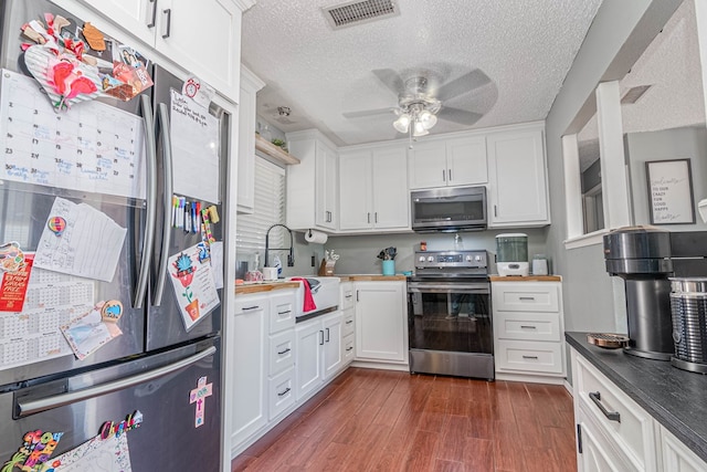 kitchen with visible vents, dark wood-type flooring, a ceiling fan, stainless steel appliances, and white cabinets