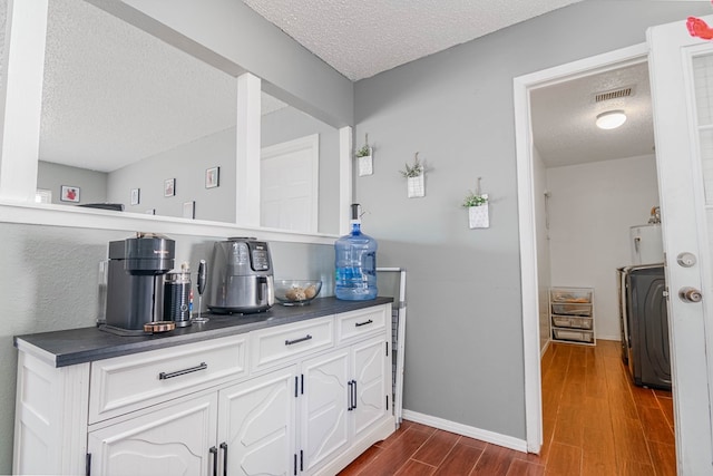 bar with visible vents, baseboards, dark wood finished floors, a textured ceiling, and washer / clothes dryer