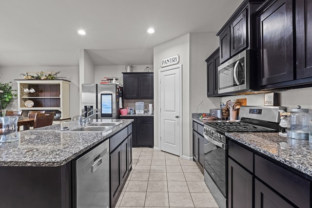 kitchen featuring light tile patterned flooring, sink, dark stone counters, stainless steel appliances, and a center island with sink