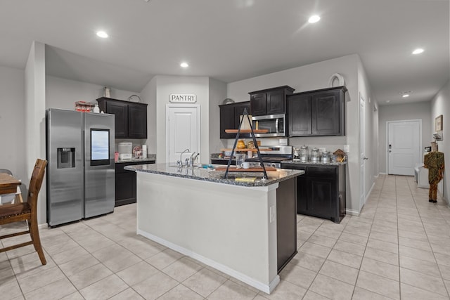 kitchen featuring light tile patterned flooring, sink, dark stone countertops, appliances with stainless steel finishes, and an island with sink