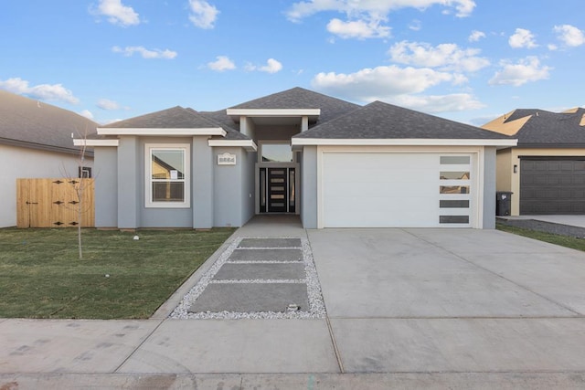 prairie-style home with stucco siding, a shingled roof, an attached garage, a front yard, and driveway