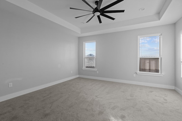 carpeted spare room featuring baseboards, a tray ceiling, and a ceiling fan