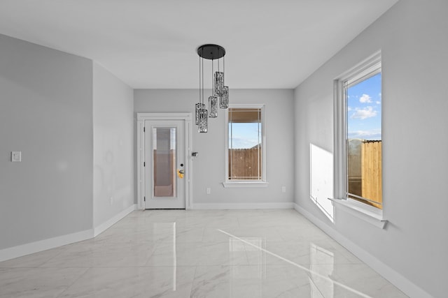 unfurnished dining area featuring a notable chandelier, marble finish floor, a wealth of natural light, and baseboards