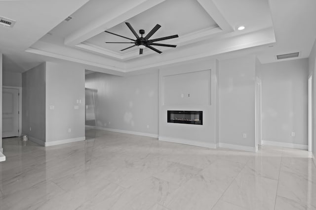 unfurnished living room with a ceiling fan, a tray ceiling, a glass covered fireplace, and visible vents