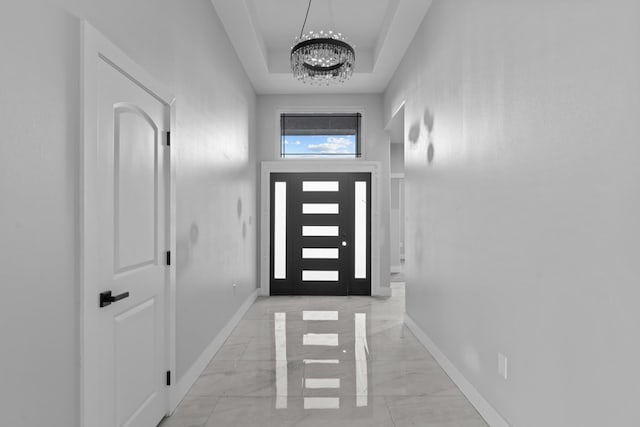 doorway featuring marble finish floor, baseboards, a raised ceiling, and a notable chandelier