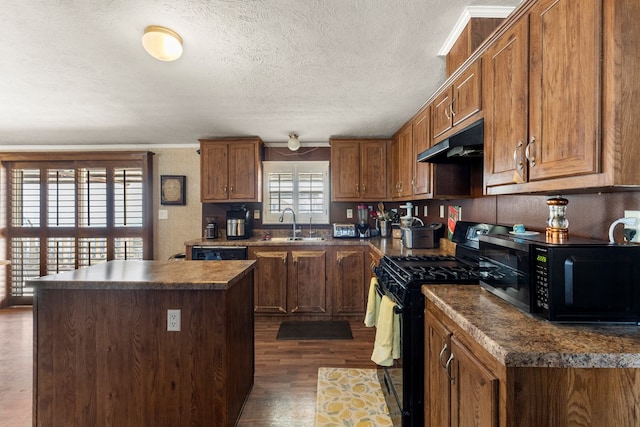 kitchen with dark countertops, a center island, under cabinet range hood, black appliances, and a sink