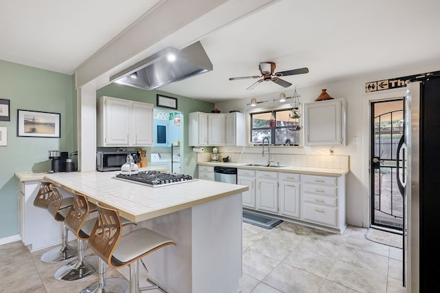 kitchen with tile counters, appliances with stainless steel finishes, a kitchen breakfast bar, and white cabinets