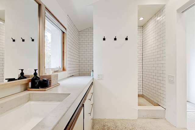 bathroom with vanity, tiled shower, and vaulted ceiling