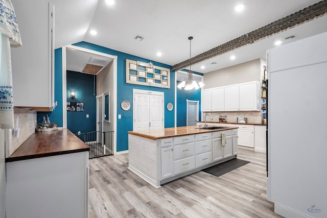 kitchen with a center island with sink, sink, light hardwood / wood-style flooring, white cabinetry, and butcher block counters