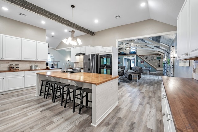 kitchen with butcher block counters, white cabinetry, sink, stainless steel fridge, and vaulted ceiling