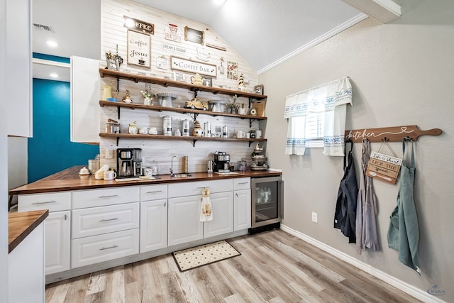 bar with lofted ceiling, wooden counters, ornamental molding, white cabinetry, and beverage cooler