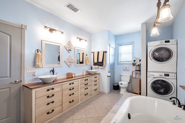 bathroom with vanity, a bath, tile patterned flooring, toilet, and stacked washer / drying machine