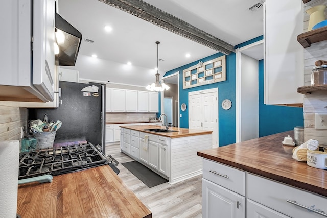 kitchen featuring wooden counters, light wood-type flooring, sink, white cabinets, and hanging light fixtures