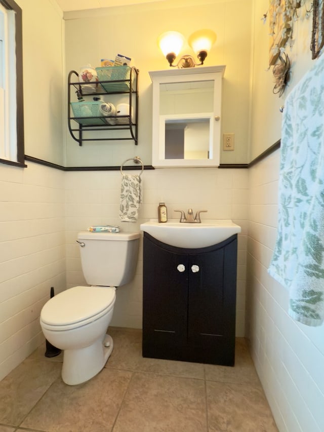 half bathroom with tile patterned floors, toilet, tile walls, wainscoting, and vanity