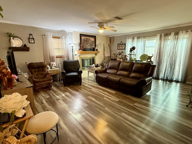 living room featuring wood finished floors, visible vents, a fireplace, ceiling fan, and crown molding