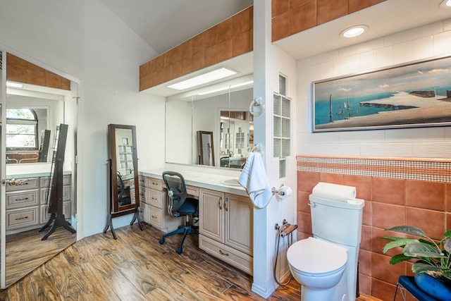 bathroom featuring hardwood / wood-style flooring, tile walls, vanity, vaulted ceiling, and toilet