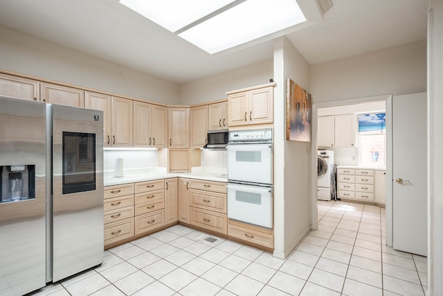 kitchen with light tile patterned flooring, appliances with stainless steel finishes, a skylight, washer / clothes dryer, and light brown cabinets