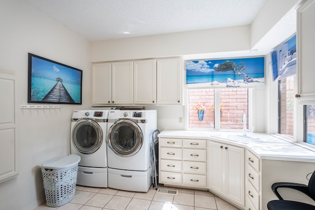 clothes washing area with sink, light tile patterned floors, washing machine and dryer, cabinets, and a textured ceiling