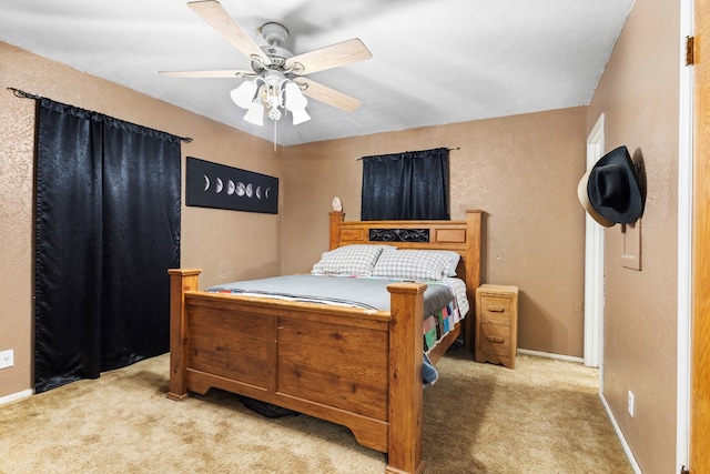 bedroom with ceiling fan, a textured wall, baseboards, and light colored carpet