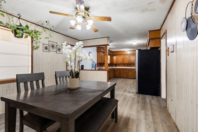 dining room featuring wooden walls, light wood-type flooring, ceiling fan, and a textured ceiling