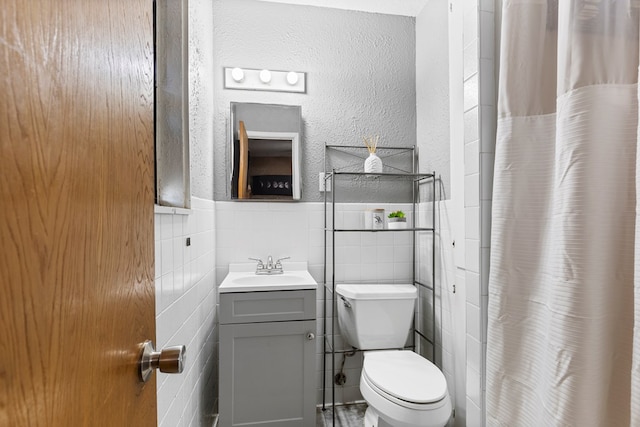 bathroom featuring toilet, a textured wall, tile walls, and vanity