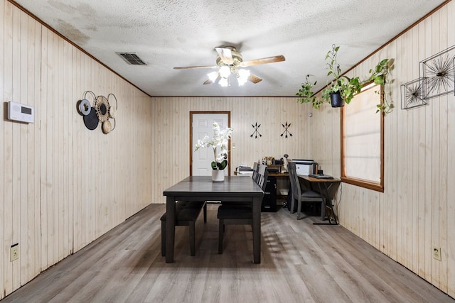 dining area with light wood-style floors, visible vents, a textured ceiling, and ornamental molding