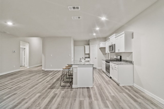 kitchen featuring stainless steel appliances, light stone counters, white cabinetry, and an island with sink