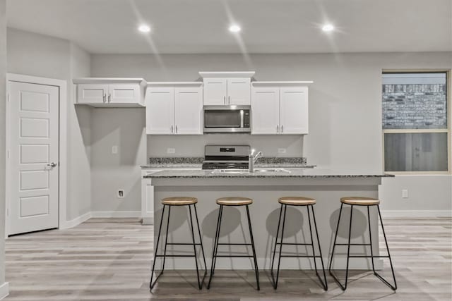 kitchen with white cabinetry, light stone countertops, sink, a kitchen bar, and a center island with sink