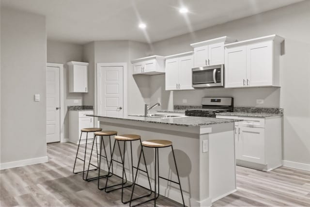 kitchen with sink, white cabinetry, white range with gas cooktop, and an island with sink