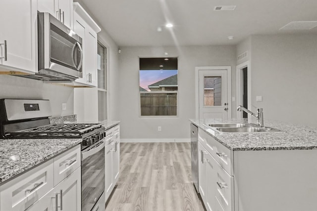 kitchen with appliances with stainless steel finishes, light stone counters, a kitchen island with sink, sink, and white cabinets