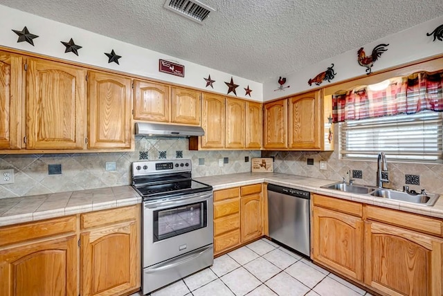 kitchen with light tile patterned flooring, sink, tile countertops, stainless steel appliances, and decorative backsplash