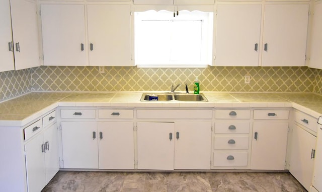 kitchen featuring tasteful backsplash, white cabinetry, sink, and tile counters