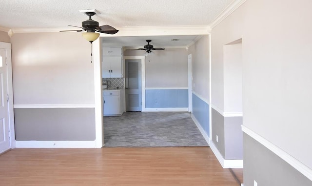 interior space featuring a textured ceiling, light wood-type flooring, ceiling fan, and crown molding