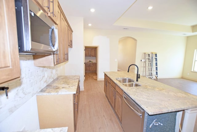 kitchen with a center island with sink, sink, decorative backsplash, light wood-type flooring, and appliances with stainless steel finishes