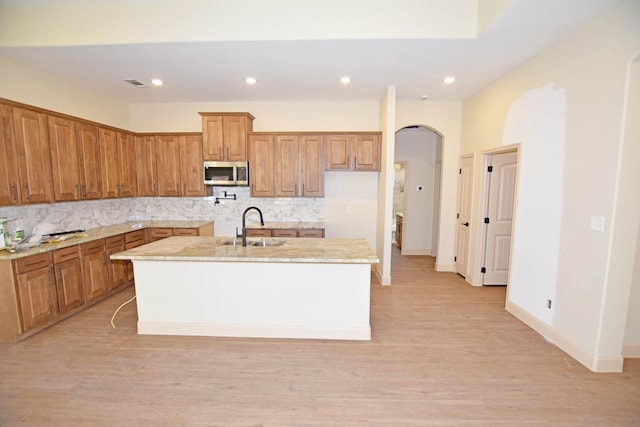 kitchen featuring decorative backsplash, a center island with sink, light hardwood / wood-style flooring, and sink