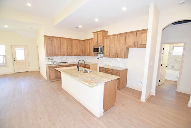 kitchen with sink, light stone countertops, an island with sink, and light hardwood / wood-style flooring