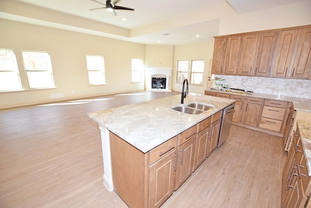 kitchen with sink, tasteful backsplash, stainless steel dishwasher, light hardwood / wood-style floors, and a kitchen island with sink