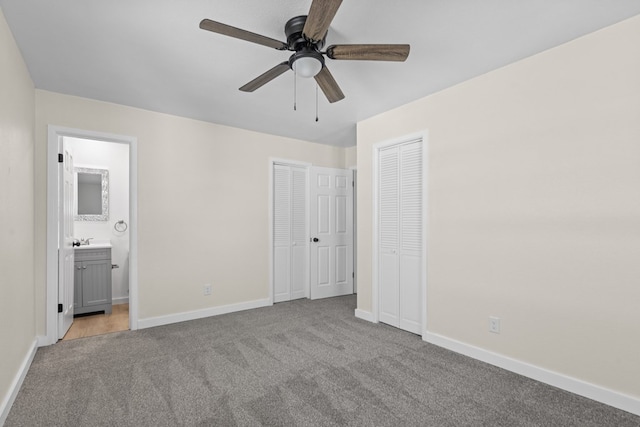 unfurnished bedroom featuring two closets, sink, ceiling fan, light carpet, and ensuite bath