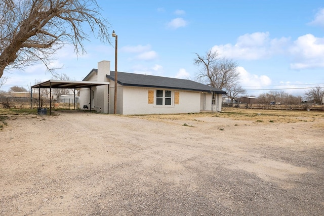 view of side of home with dirt driveway, a chimney, and fence