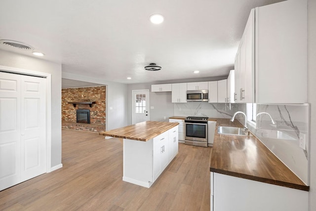 kitchen with a sink, a kitchen island, wood counters, white cabinets, and appliances with stainless steel finishes