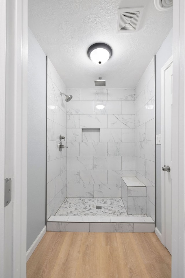 bathroom featuring a textured ceiling, visible vents, a tile shower, and wood finished floors