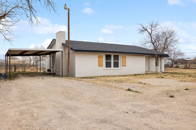 view of side of property featuring brick siding, a chimney, dirt driveway, fence, and a carport